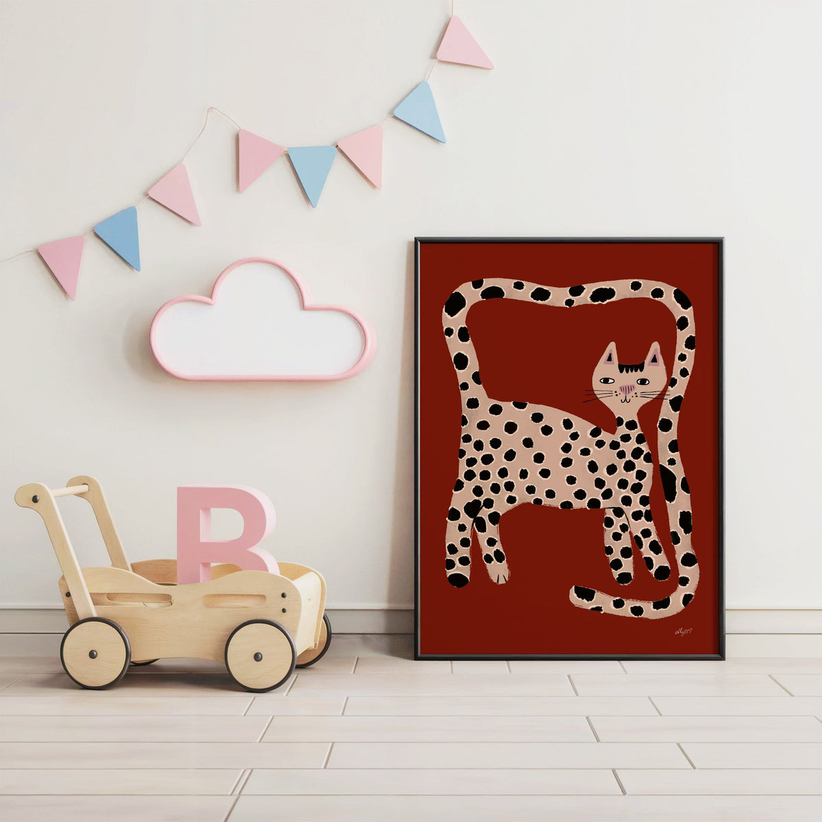 Spotted cat with looping tail nursery print in a black frame under pastel bunting by a wooden baby walker