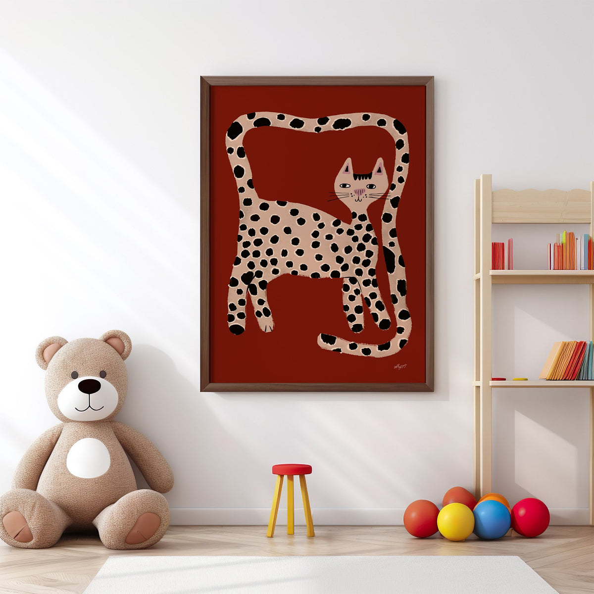 Spotted cat with looping tail nursery print in a walnut frame above a big teddy bear by a bookshelf