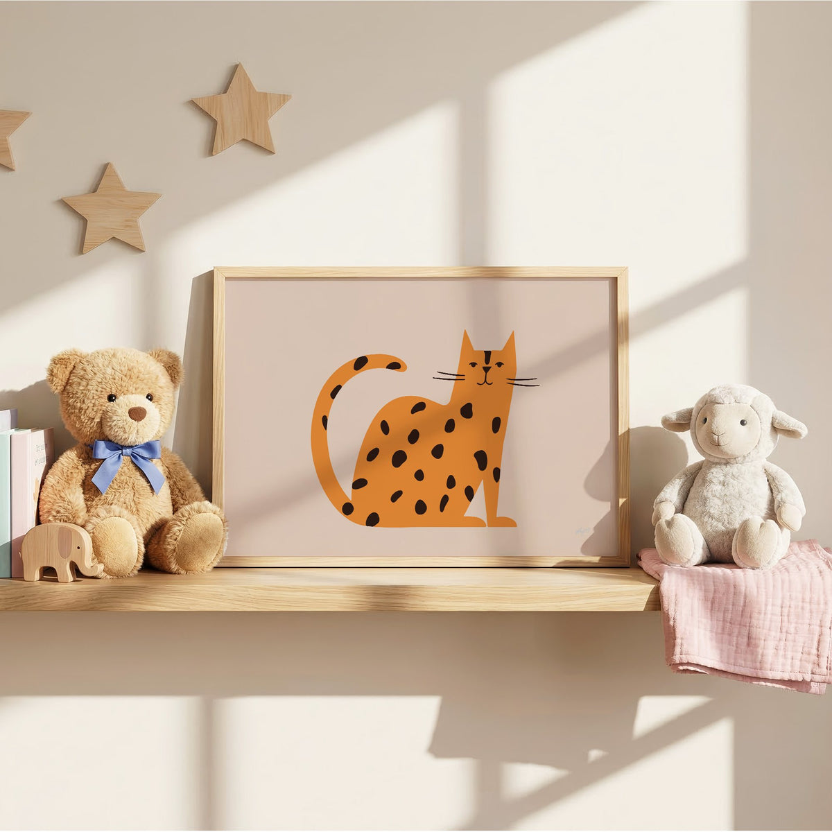 Minimal orange spotted cat nursery print in an oak frame on a wall shelf between a teddy bear and a toy lamb