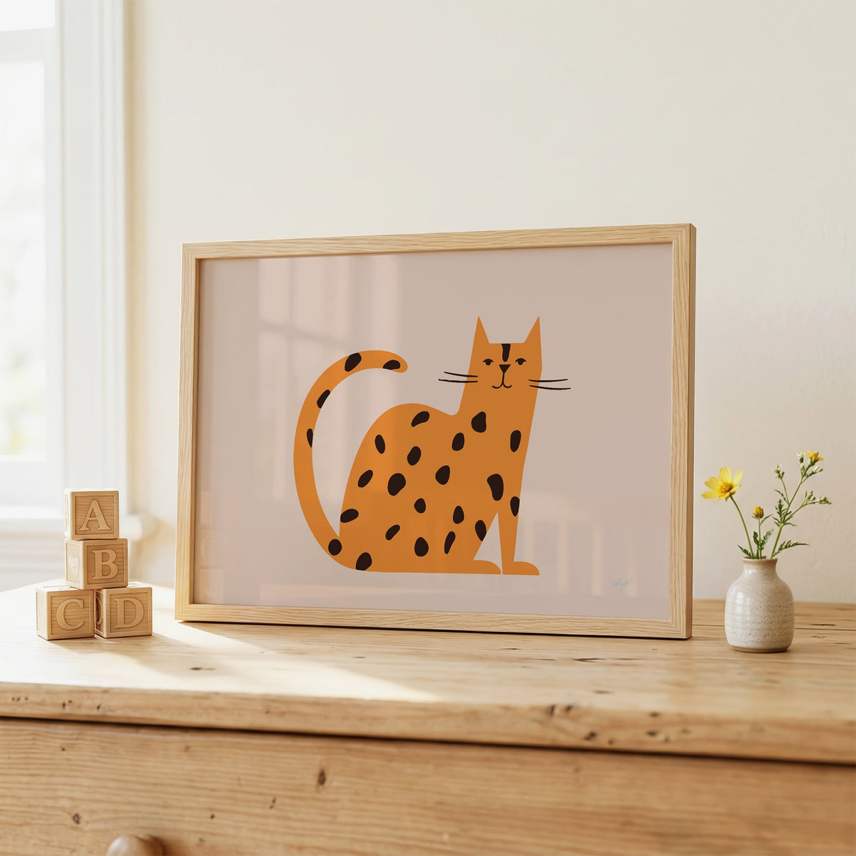 Minimal orange spotted cat nursery print in an oak frame on a wooden dresser beside ABC blocks