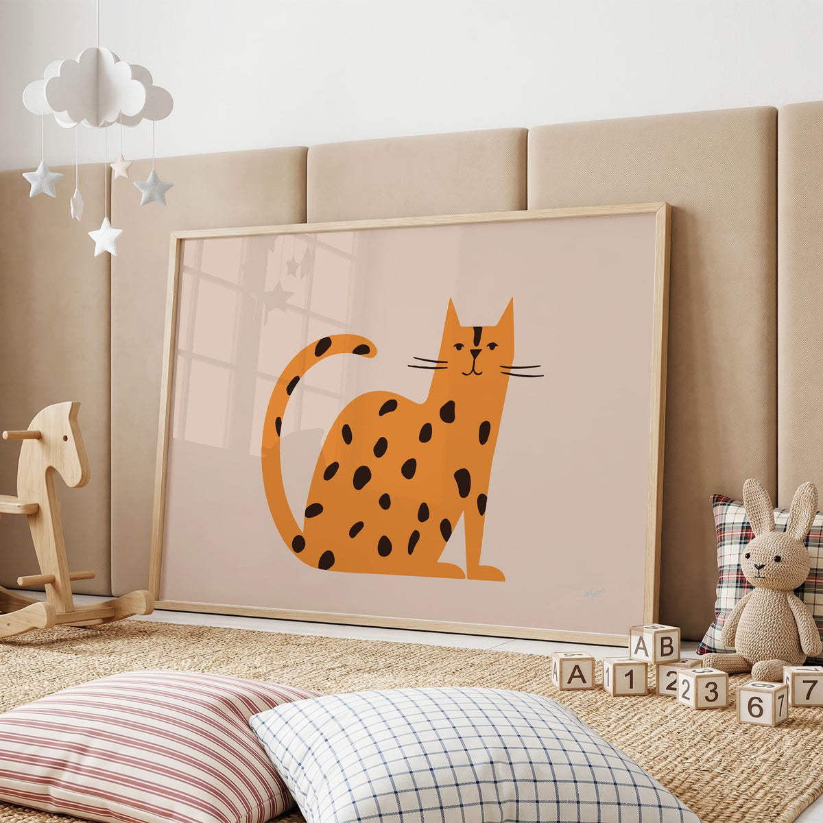 Minimal orange spotted cat nursery print in an oak frame on a padded wall by a wooden rocking horse