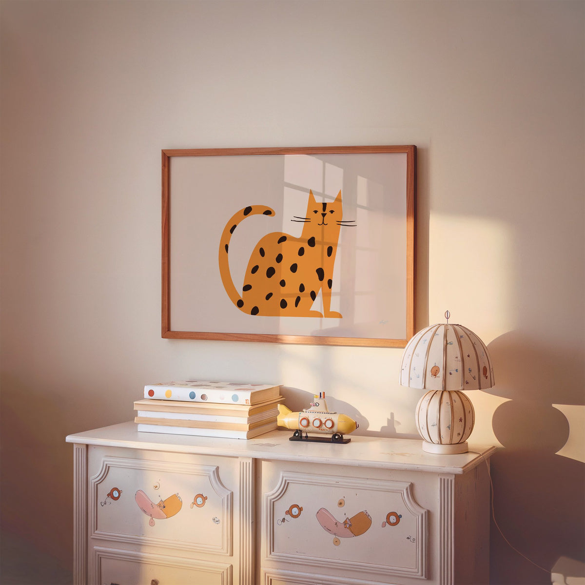 Minimal orange spotted cat nursery print in a cherry wood frame above a painted dresser and lamp