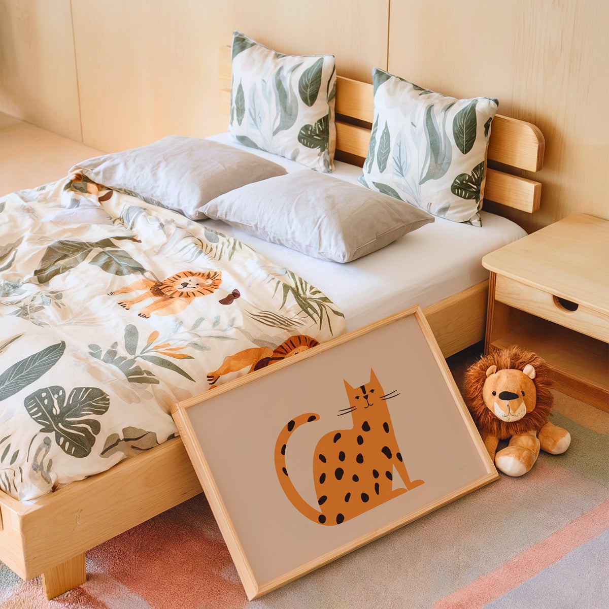 Minimal orange spotted cat nursery print in an oak frame leaning on a kids bed by a lion plush