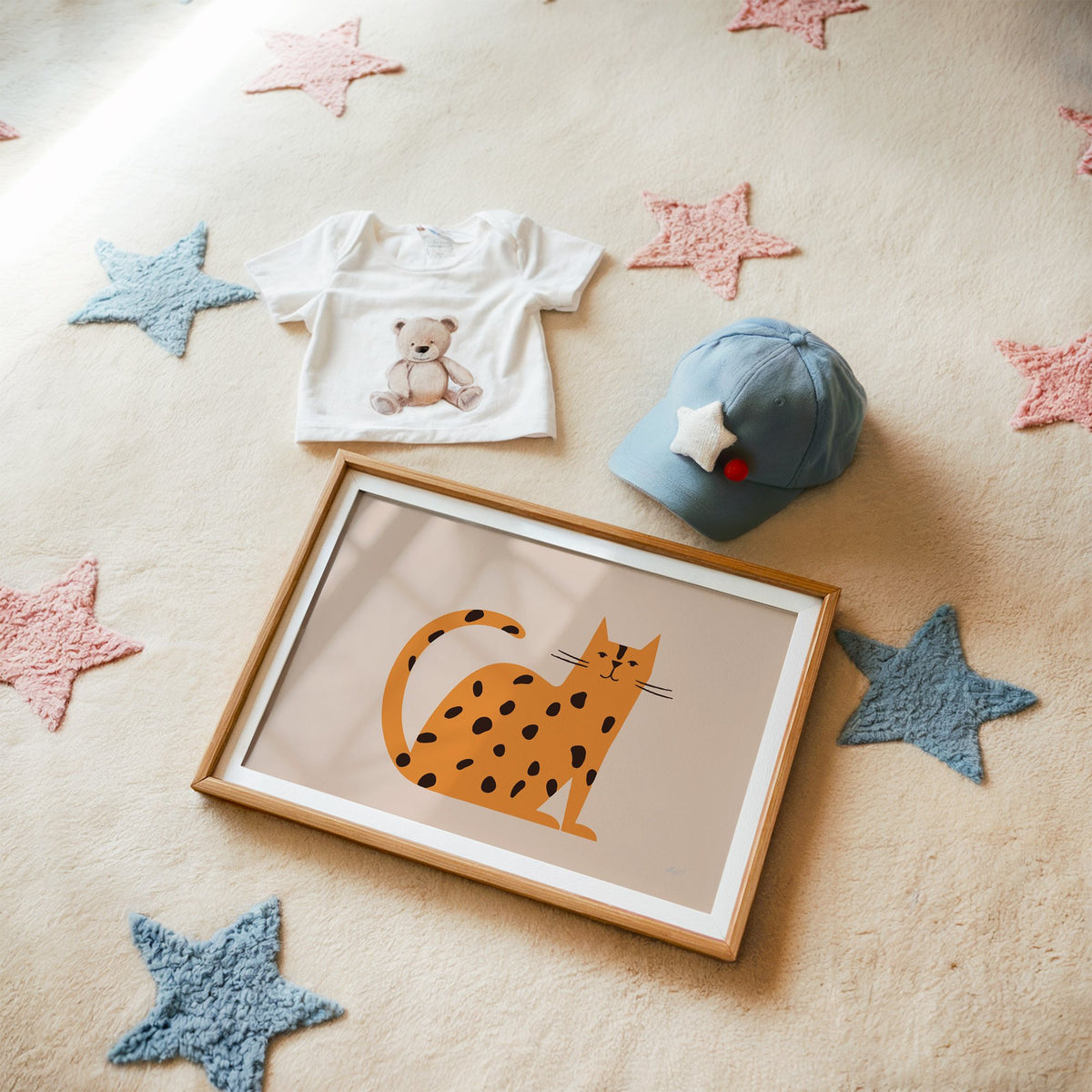 Minimal orange spotted cat nursery print in a matted oak frame on a star rug with a baby tee
