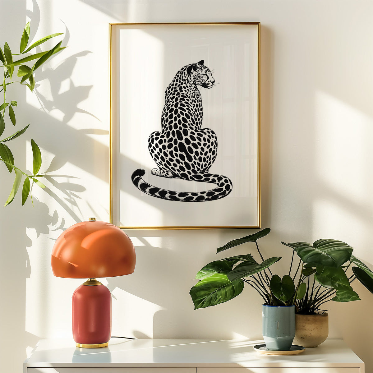 Spotted big cat seen from behind in black ink print shown in a gold frame above a white sideboard with an orange lamp