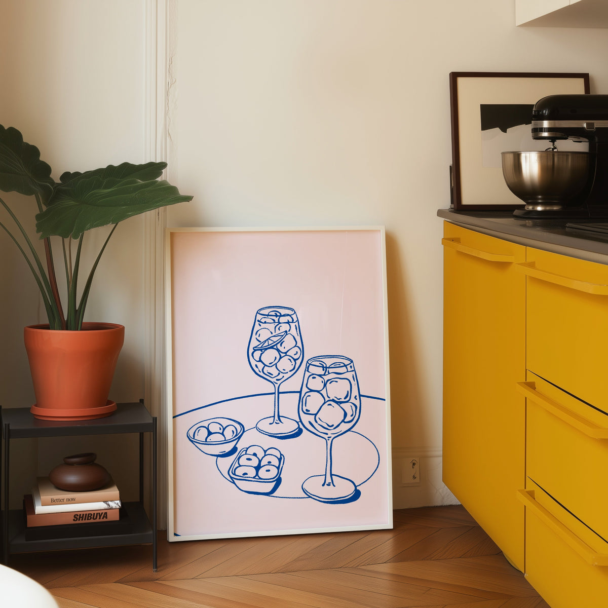 Spritz and olives print in a white frame on parquet beside a bright yellow kitchen