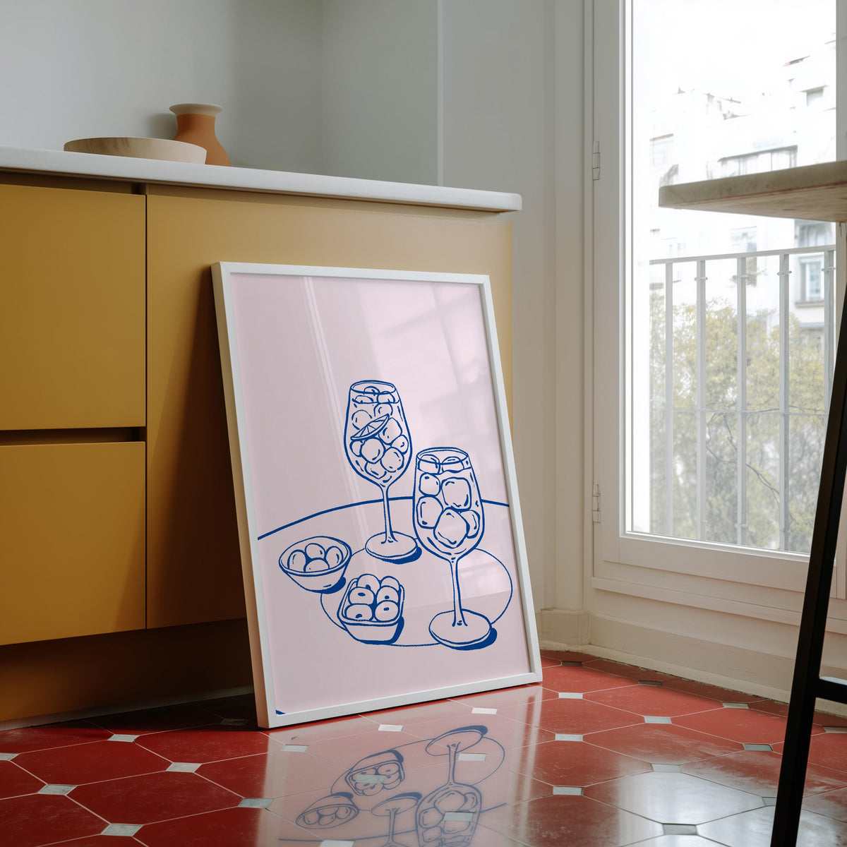 Spritz and olives print in a white frame against yellow cabinets on red tiles