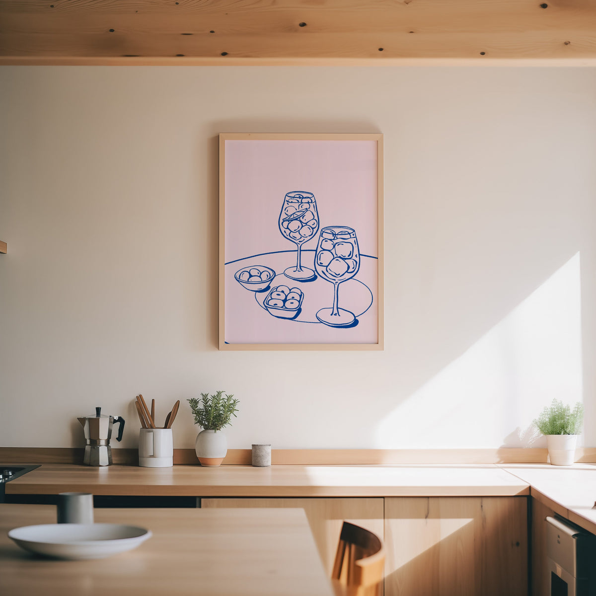Spritz and olives print in an oak frame above a wood counter with a moka pot