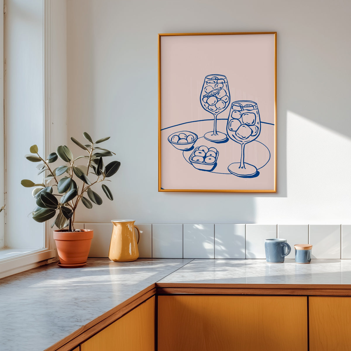 Spritz and olives print in a gold frame above a marble counter with a yellow jug