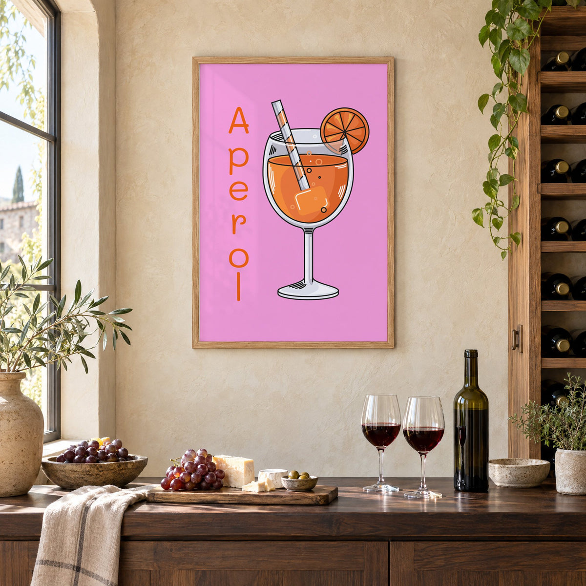 Orange spritz glass on pink print in an oak frame on a limewashed wall above a wine counter with red wine, cheese and grapes