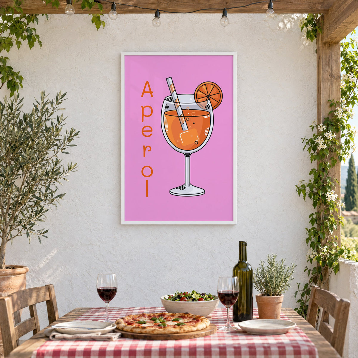 Orange spritz glass on pink print in a white frame on a stucco wall above a checked-cloth table with pizza and red wine