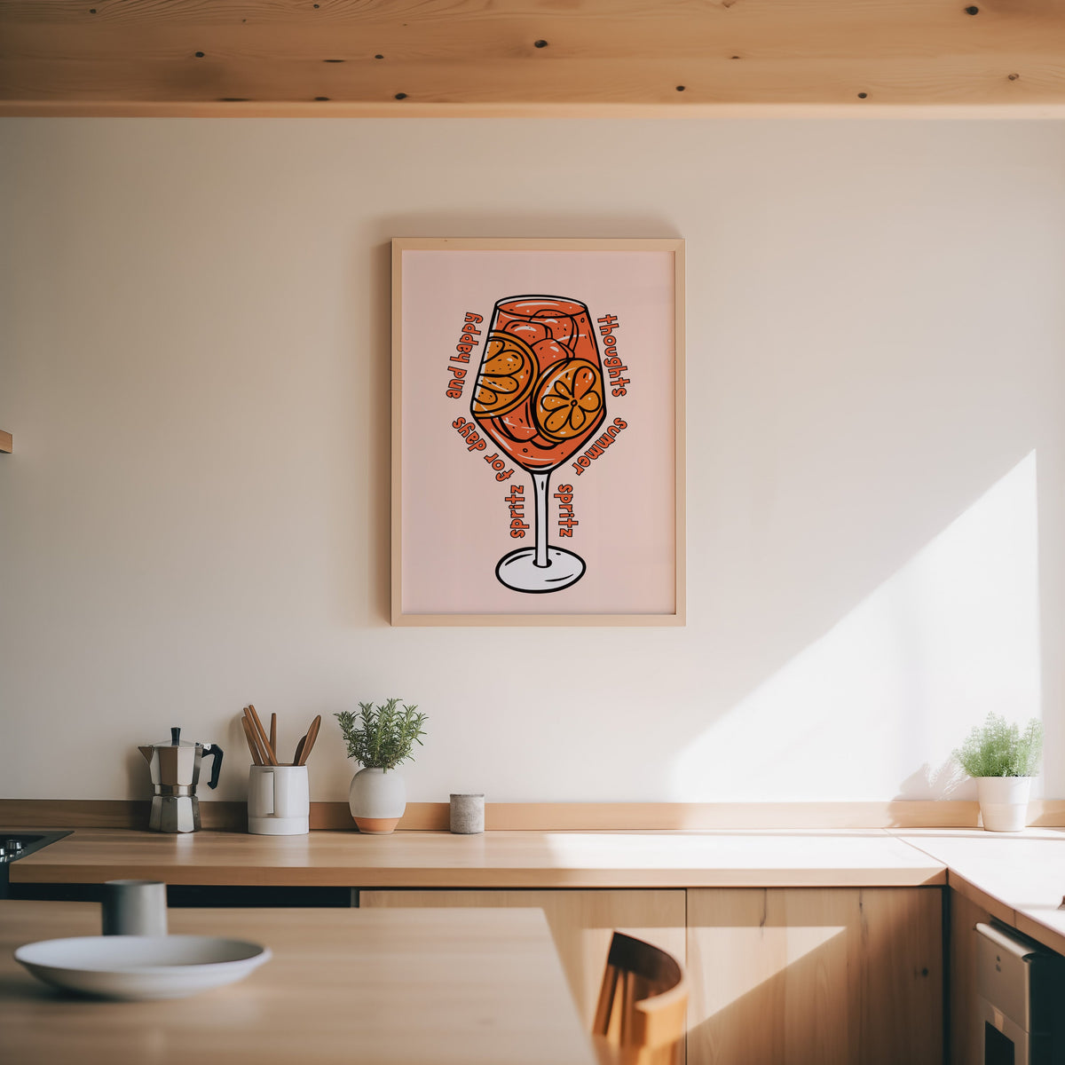 Spritz glass print in an oak frame above a wood counter with a moka pot and herbs
