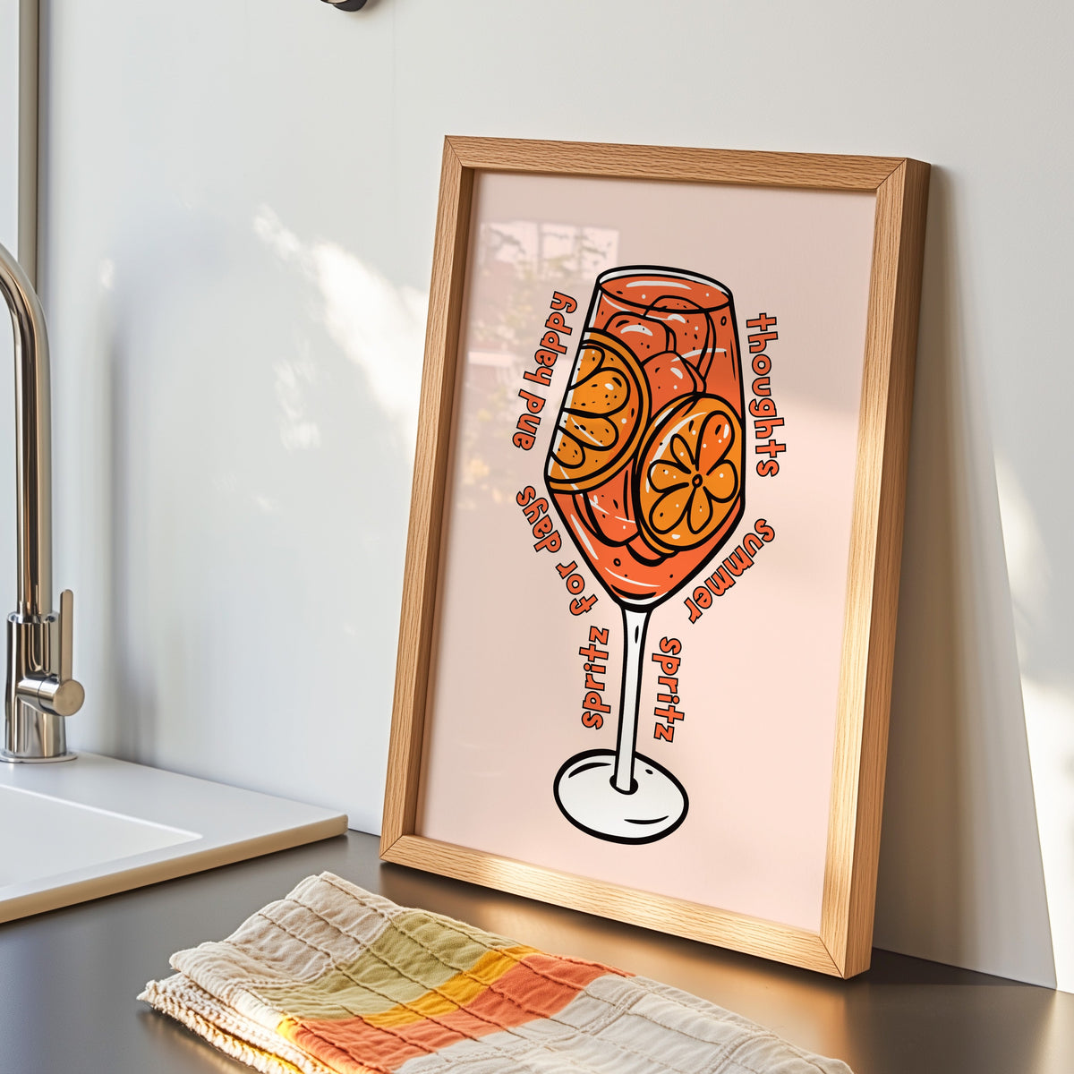 Spritz glass print in an oak frame by the kitchen sink beside a striped tea towel