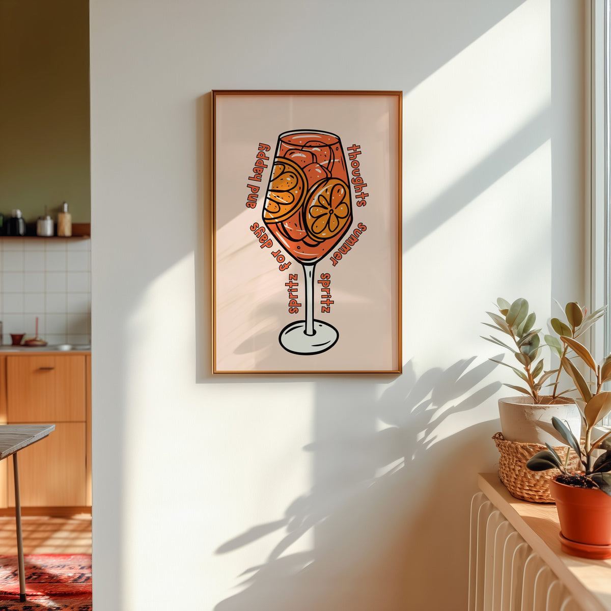 Spritz glass print in a gold frame in sunlight with plants and a kitchen beyond