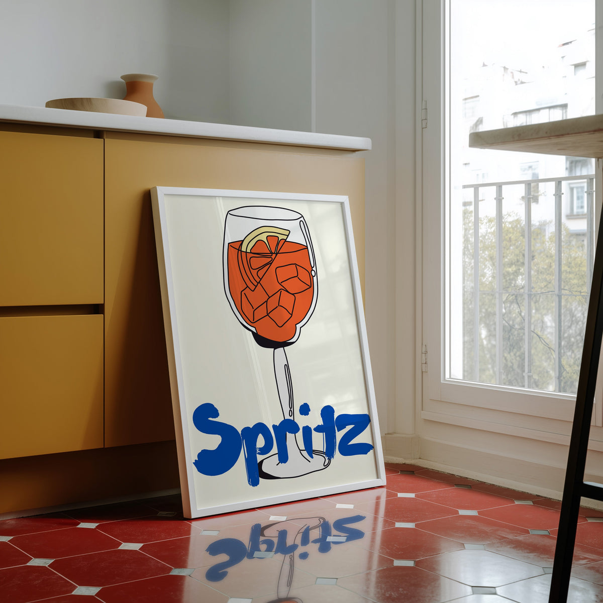 Spritz print in a white frame against yellow cabinets on a red tiled floor