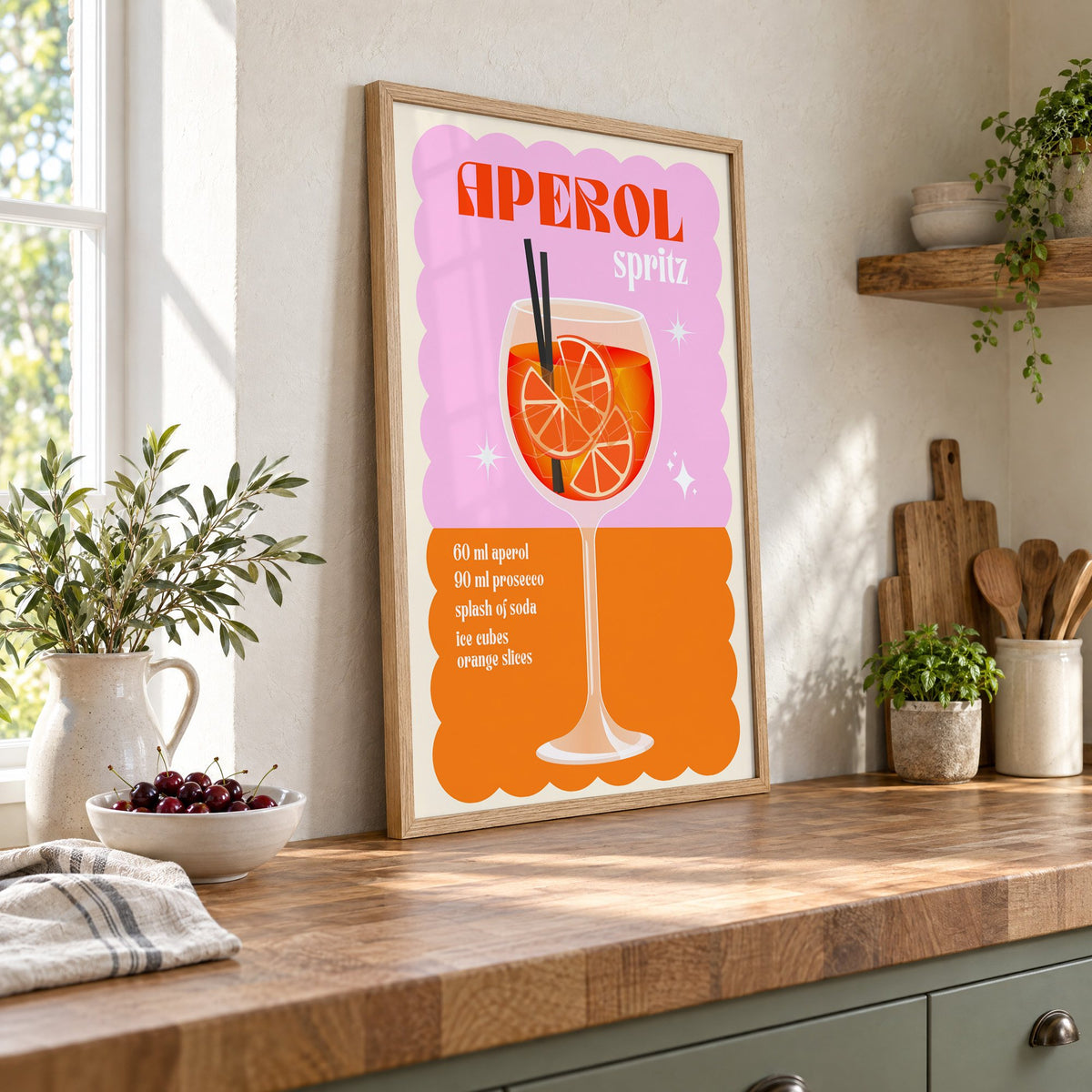 Spritz recipe pink and orange print in an oak frame leaning on a butcher block island beside a bowl of cherries
