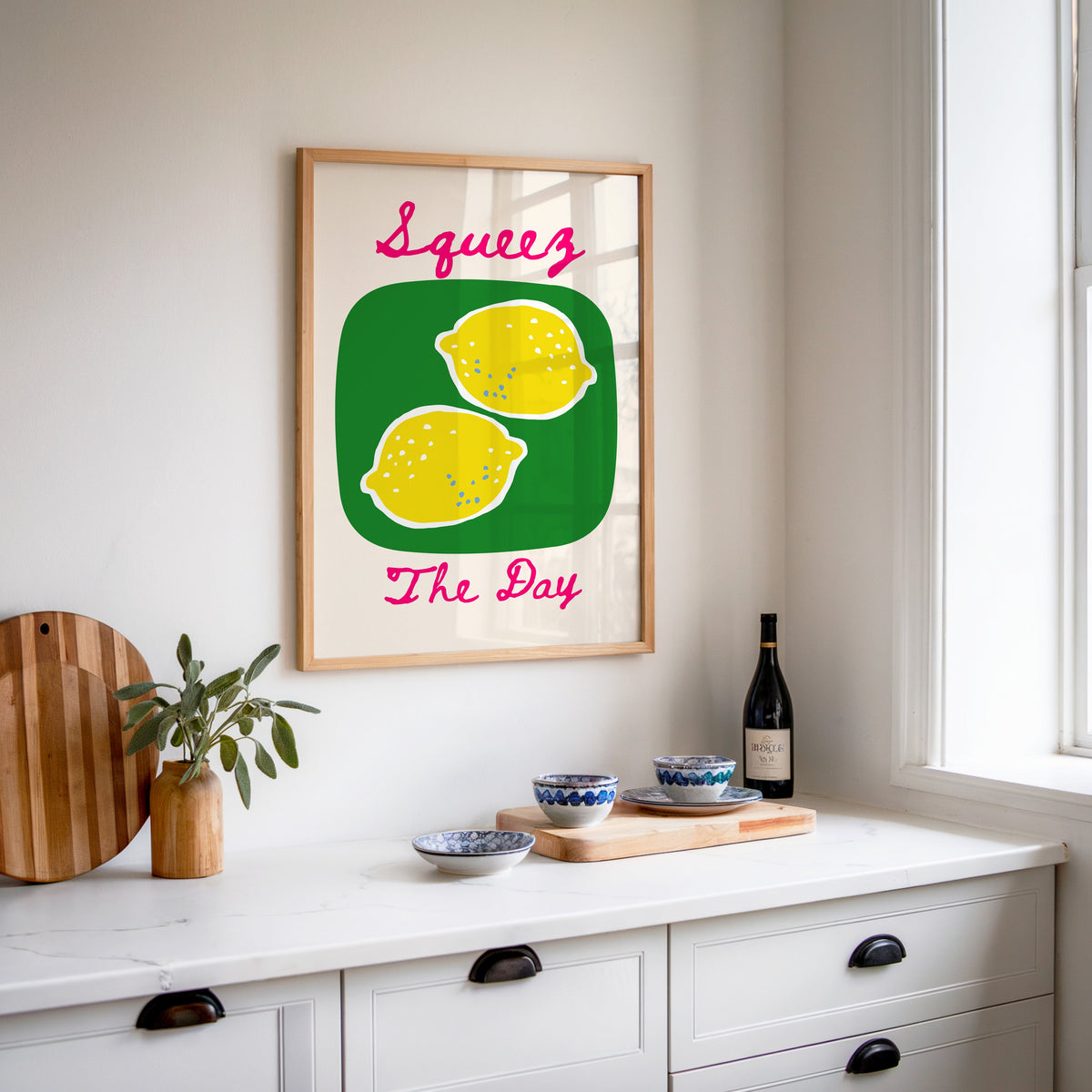 Squeez the Day lemons print in an oak frame above a white kitchen sideboard with a wine bottle and wooden board