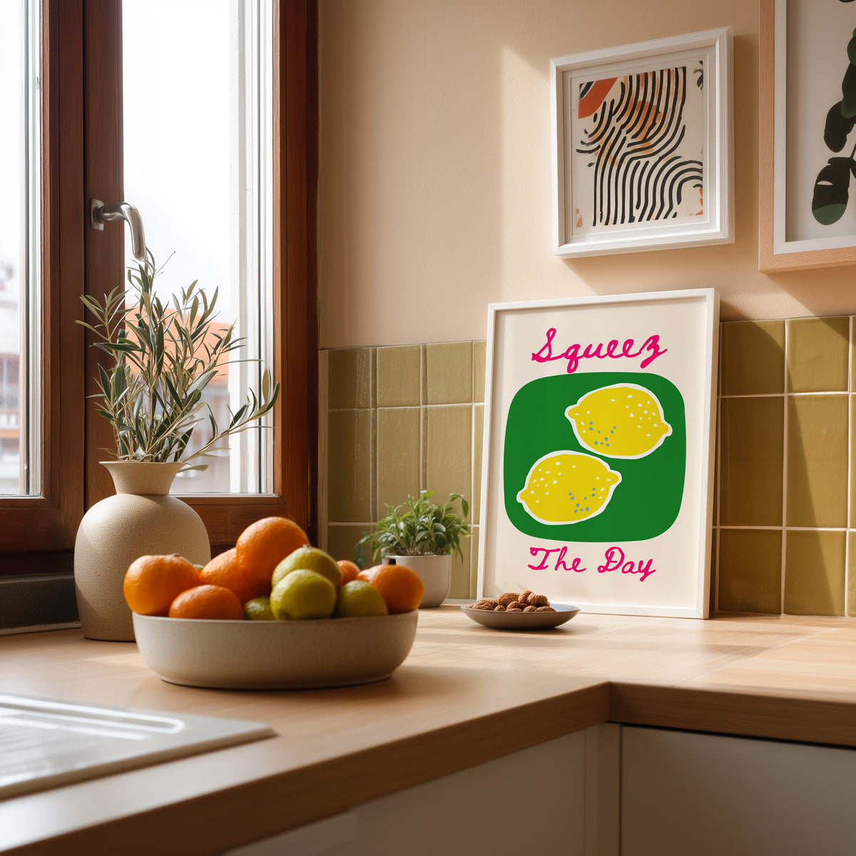 Squeez the Day lemons print in a white frame leaning against olive green kitchen tiles beside a bowl of citrus