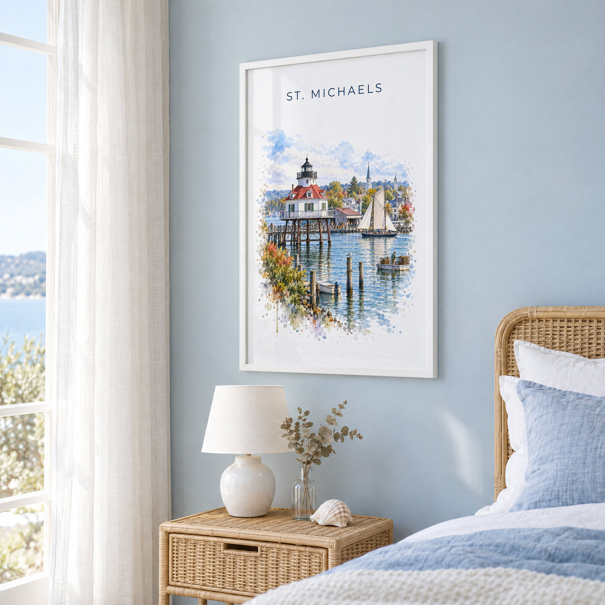 St. Michaels, Maryland watercolor print in a white frame on a pale blue wall beside a rattan bed in a coastal bedroom