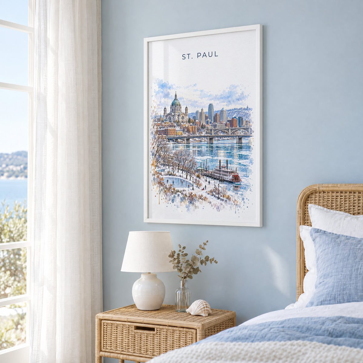 St. Paul watercolor print in a white frame on a pale blue wall beside a rattan bed in a coastal bedroom