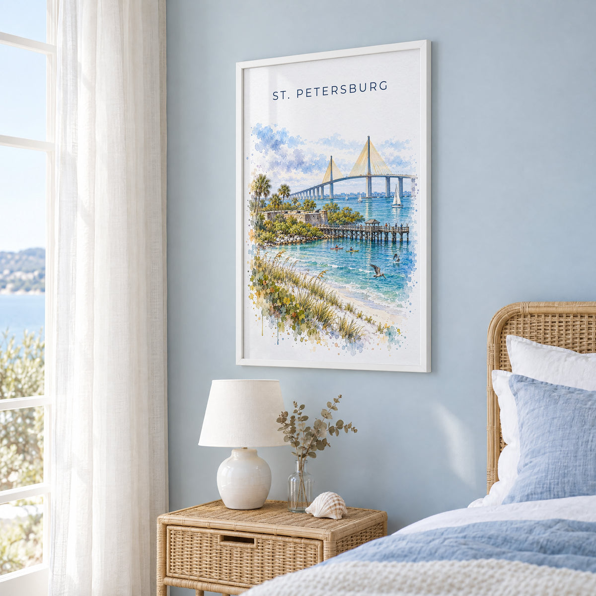 St. Petersburg, Florida watercolor print in a white frame on a pale blue wall beside a rattan bed in a coastal bedroom