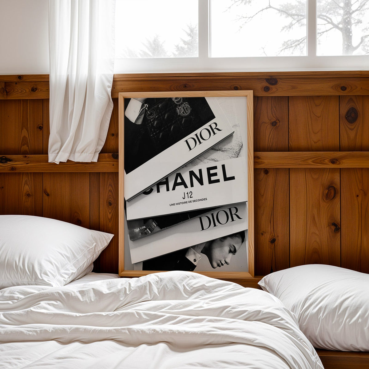 Top-down flat lay of four fashion books print in a pine frame leaning on a wood headboard over white bedding