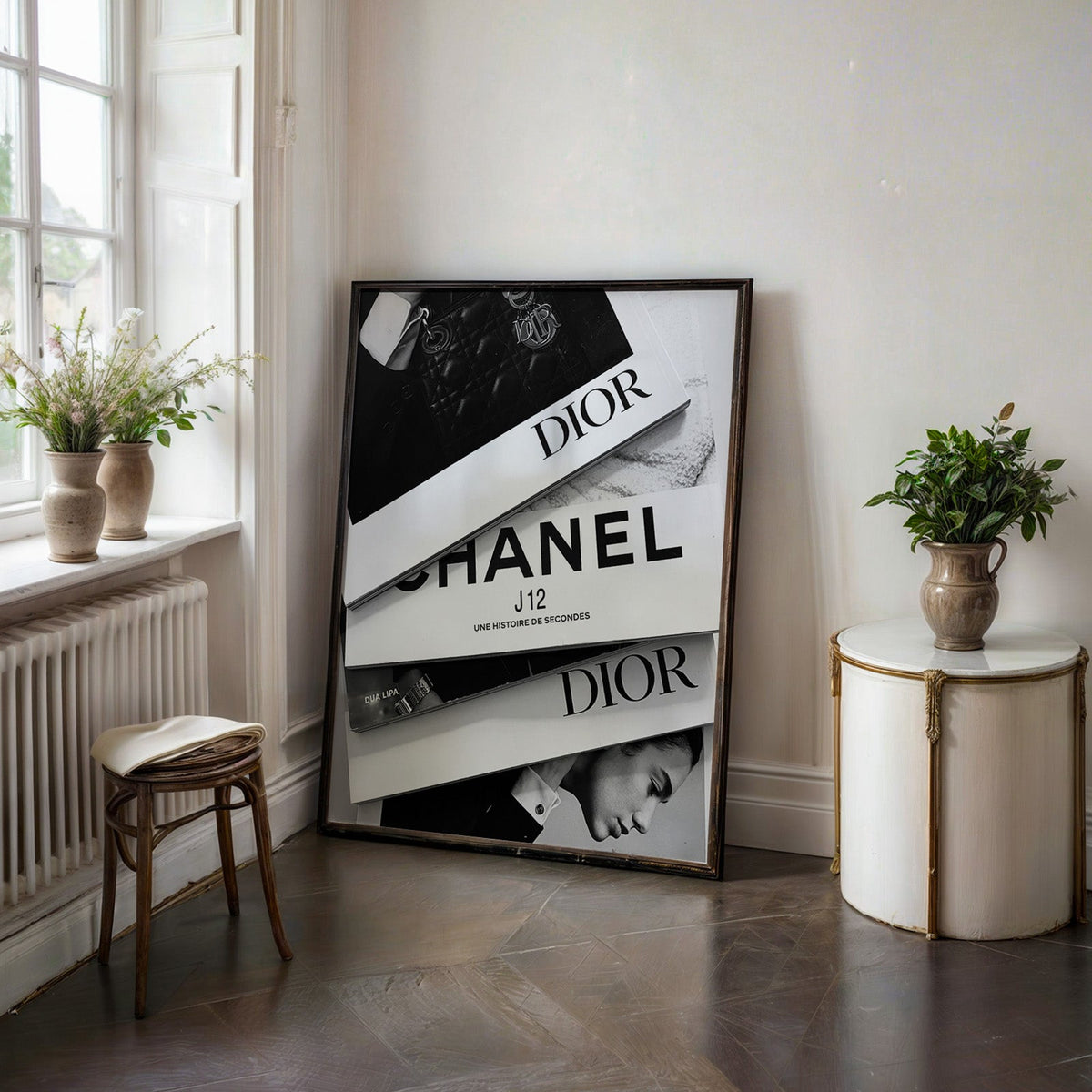 Top-down flat lay of four fashion books print in a black frame on a dark stone floor beside a white side table