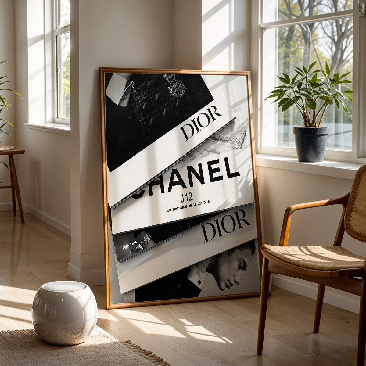 Top-down flat lay of four fashion books print in a walnut frame on a wood floor beside a cane chair and sunny window