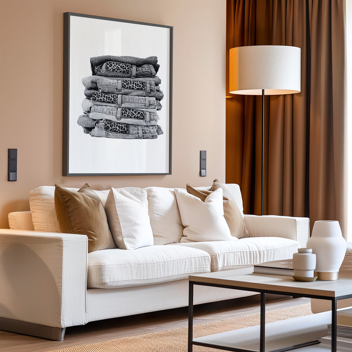 Stack of folded jeans with leopard waist patches print in a black frame above a cream sofa on a blush living room wall