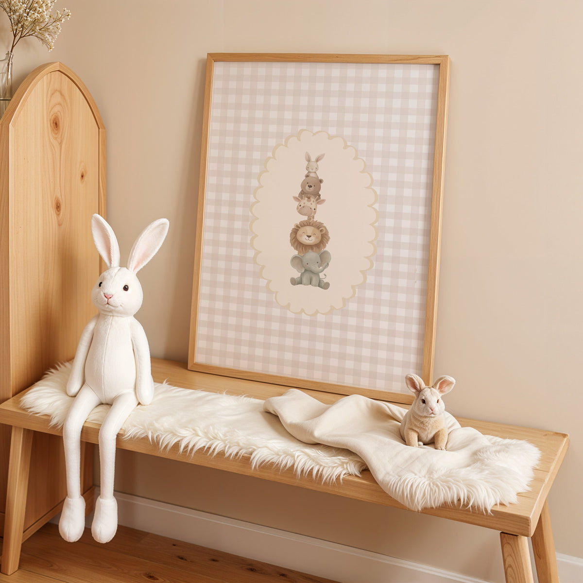 Stacked baby animals in oval on gingham nursery print in an oak frame on a sheepskin bench beside a white plush bunny