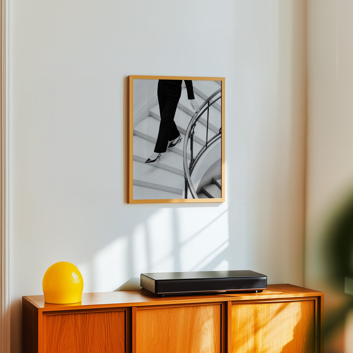 Black trousers and slingback heels on curved stairs print in an oak frame above a teak sideboard with a yellow glass lamp