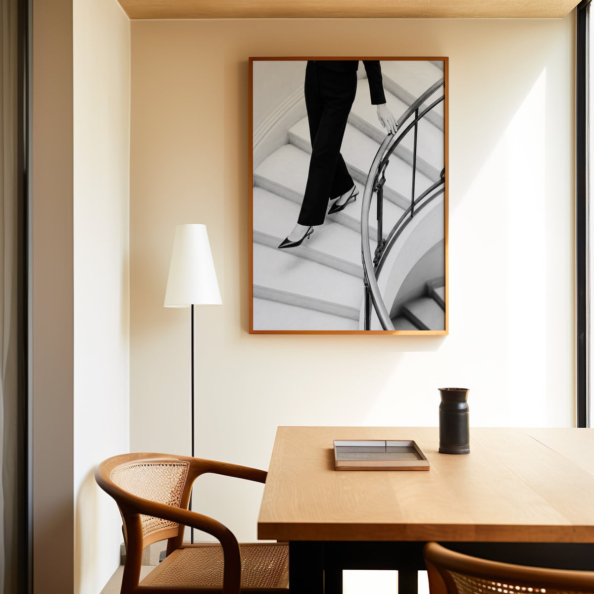 Black trousers and slingback heels on curved stairs print in an oak frame above a dining table and cane chair