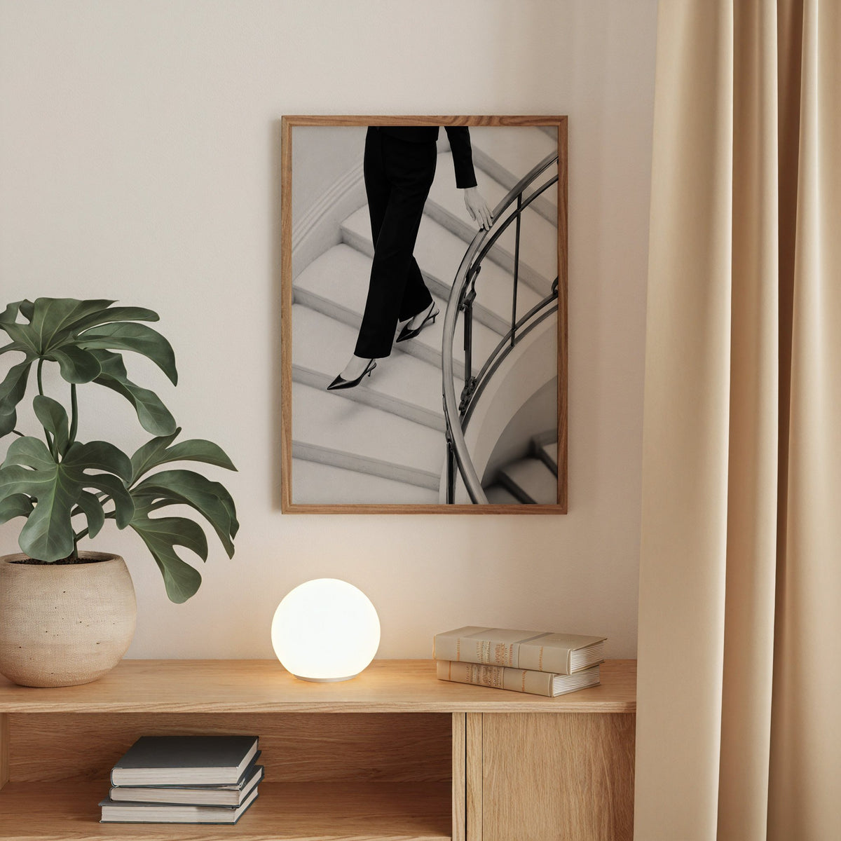 Black trousers and slingback heels on curved stairs print in a walnut frame above an oak cabinet with a glowing globe lamp