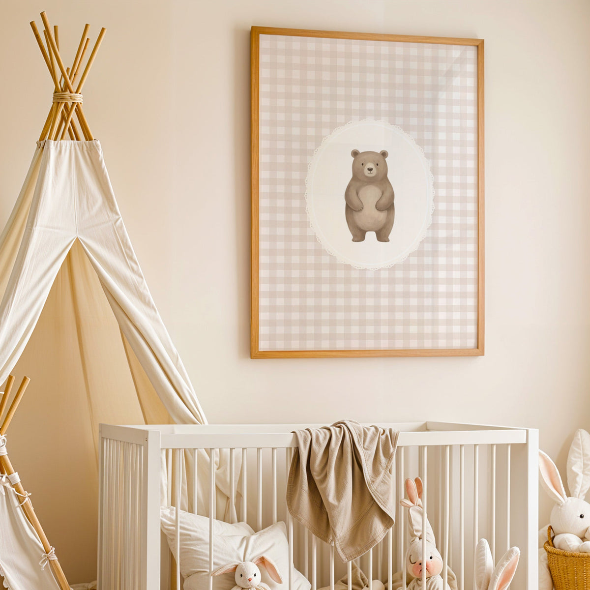 Standing bear in a lace oval on beige gingham nursery print in an oak frame above a white crib beside a canvas teepee