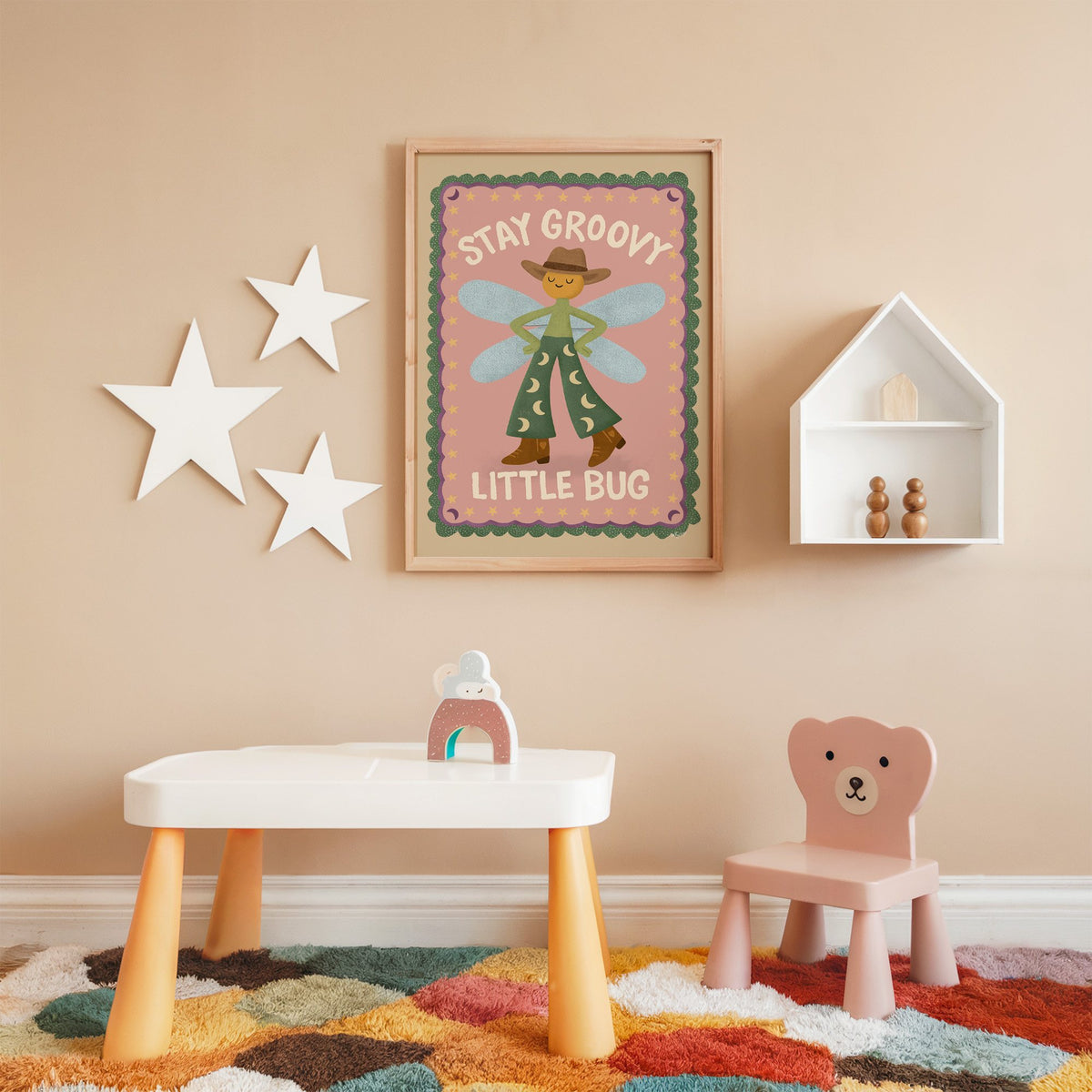Stay groovy little bug cowboy nursery print in an oak frame on a peach wall above a kids table with wall stars