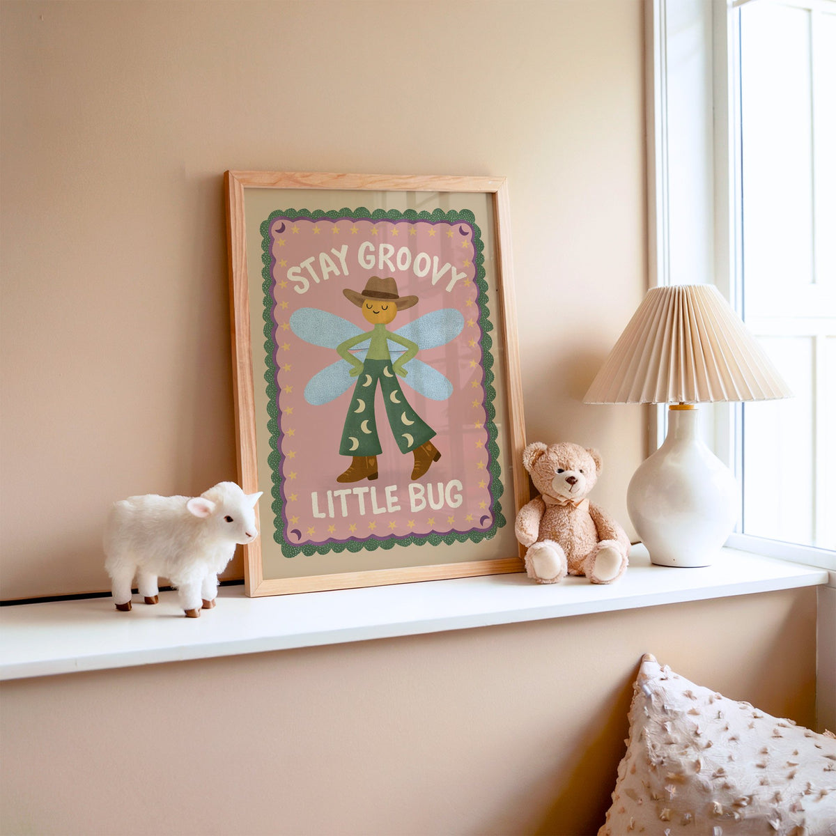 Stay groovy little bug cowboy nursery print in an oak frame on a window ledge with a toy lamb and teddy