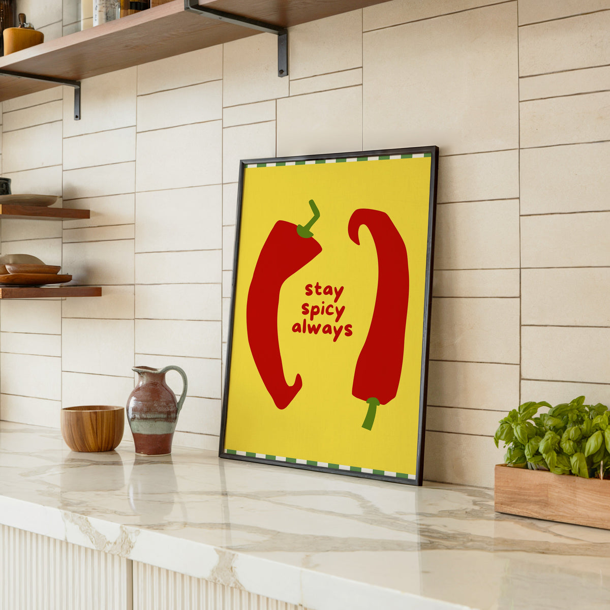 Stay Spicy Always print in a black frame leaning on a marble counter in a tiled kitchen