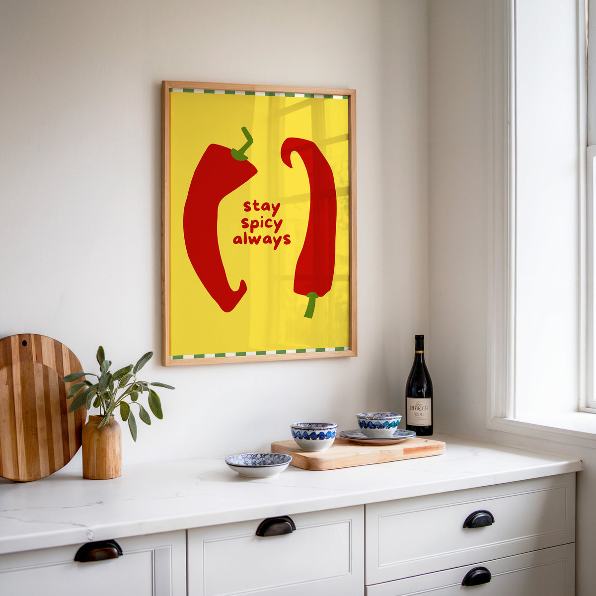 Stay Spicy Always print in an oak frame above a white sideboard with a bottle of wine