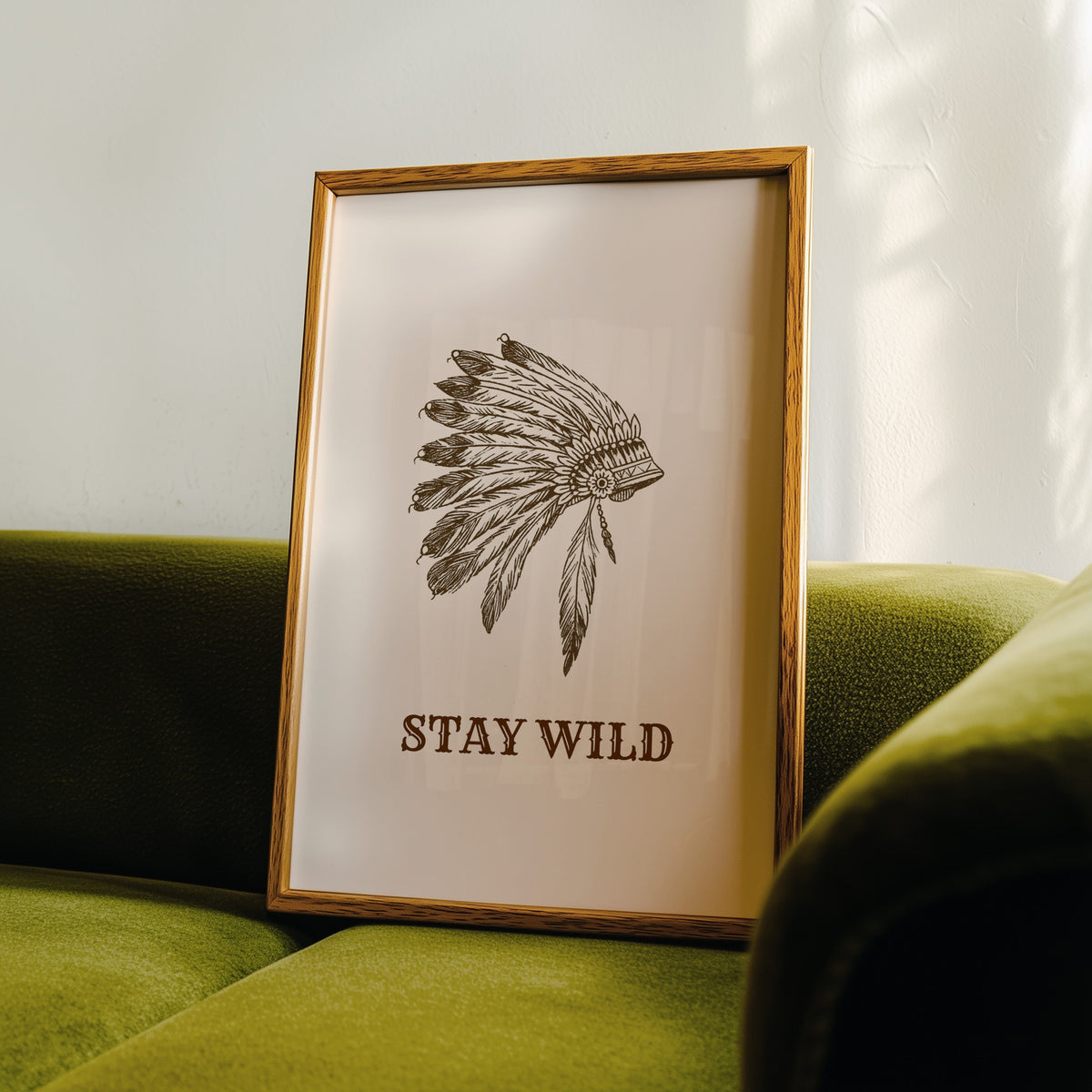 Stay Wild war bonnet cream print in an oak frame leaning on a green velvet sofa