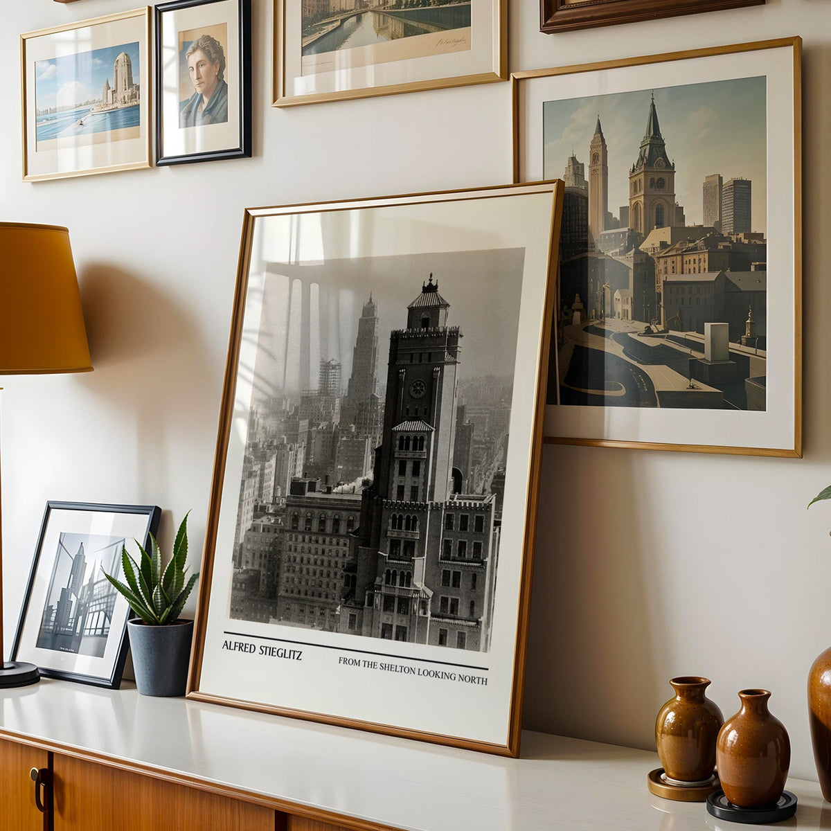 New York skyline print shown in a gold frame leaning on a sideboard in a gallery wall
