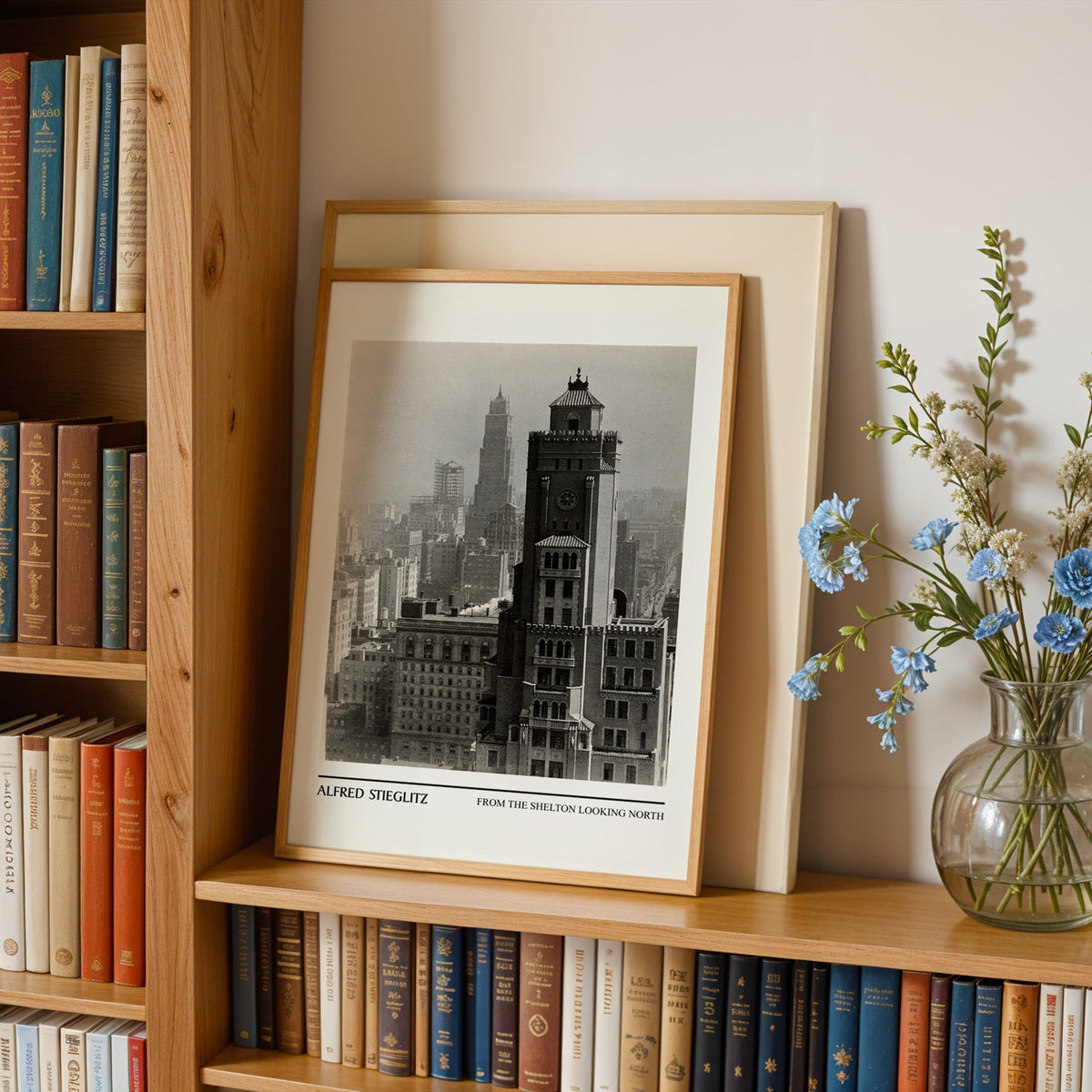 Stieglitz photography print in an oak frame leaning on a bookshelf beside flowers