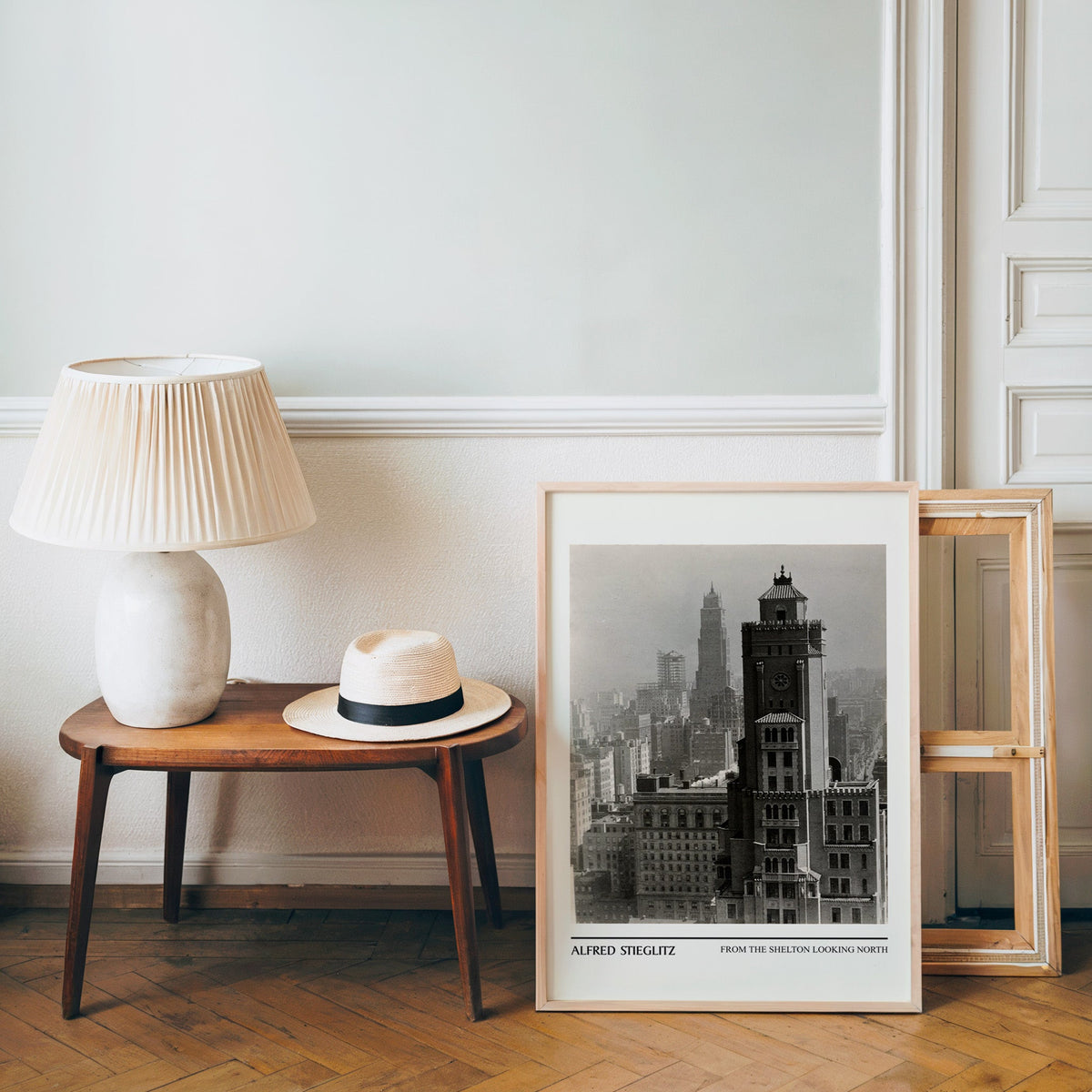 Vintage New York photo poster in a light wood frame leaning by a bench and hat