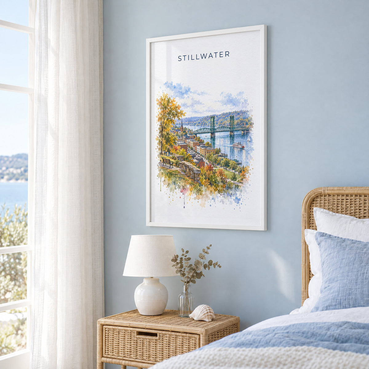 Stillwater, Minnesota watercolor print in a white frame on a pale blue wall beside a rattan bed in a coastal bedroom