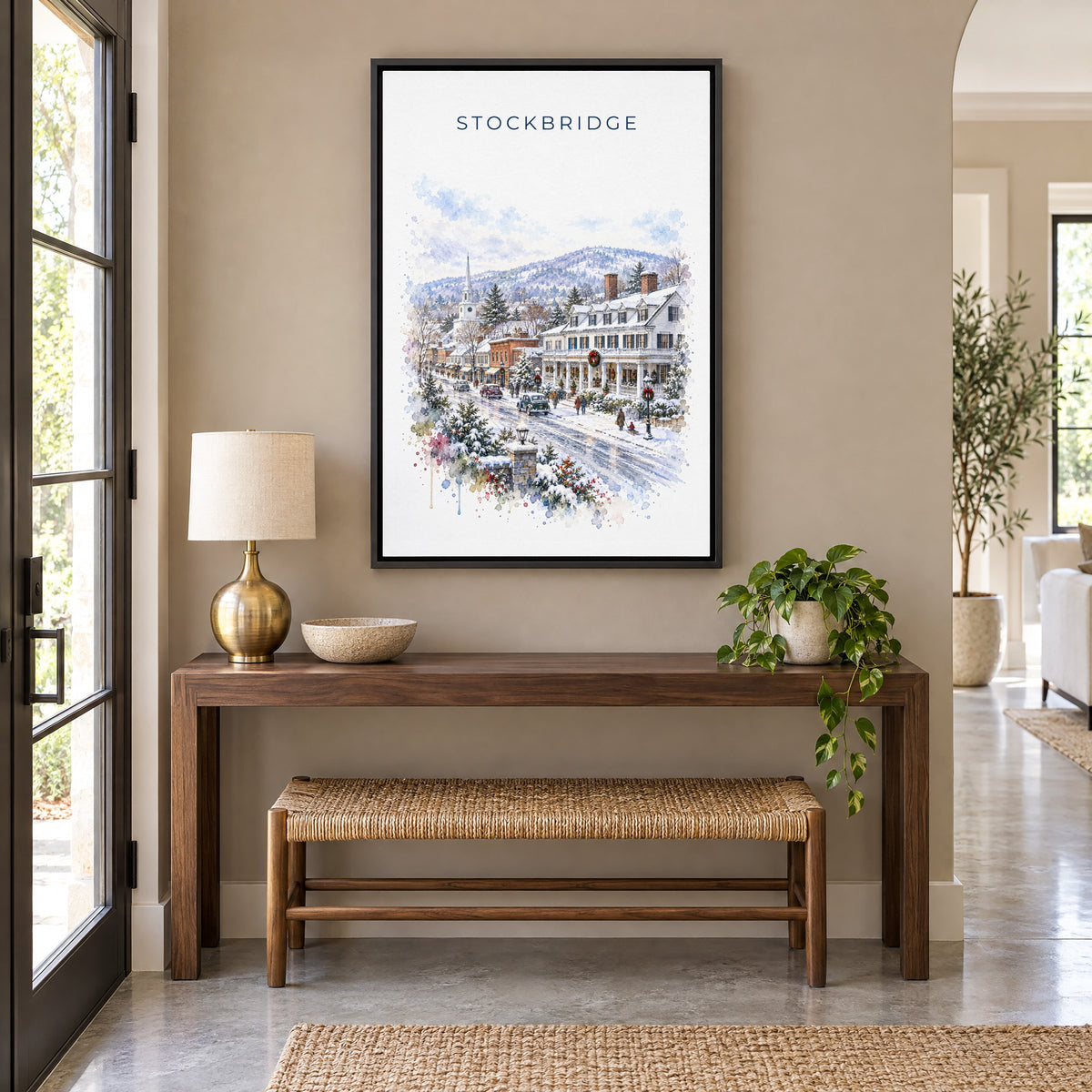 Stockbridge, Massachusetts watercolor print as a black floater canvas above a walnut console and woven bench in an entryway