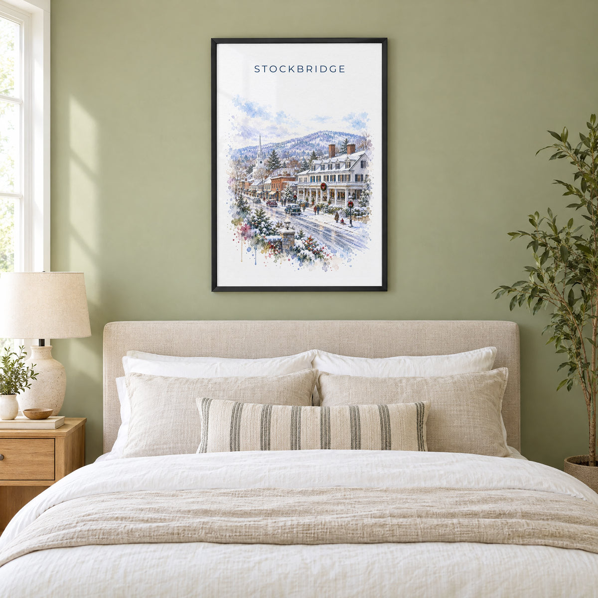 Stockbridge, Massachusetts watercolor print in a black frame above an upholstered headboard in a sage green bedroom