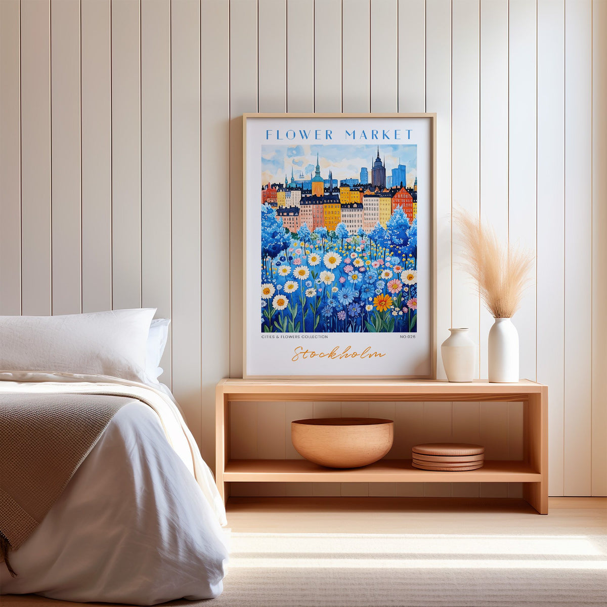 Stockholm flower market print in an oak frame on a wood bench against a white shiplap bedroom wall with pampas grass