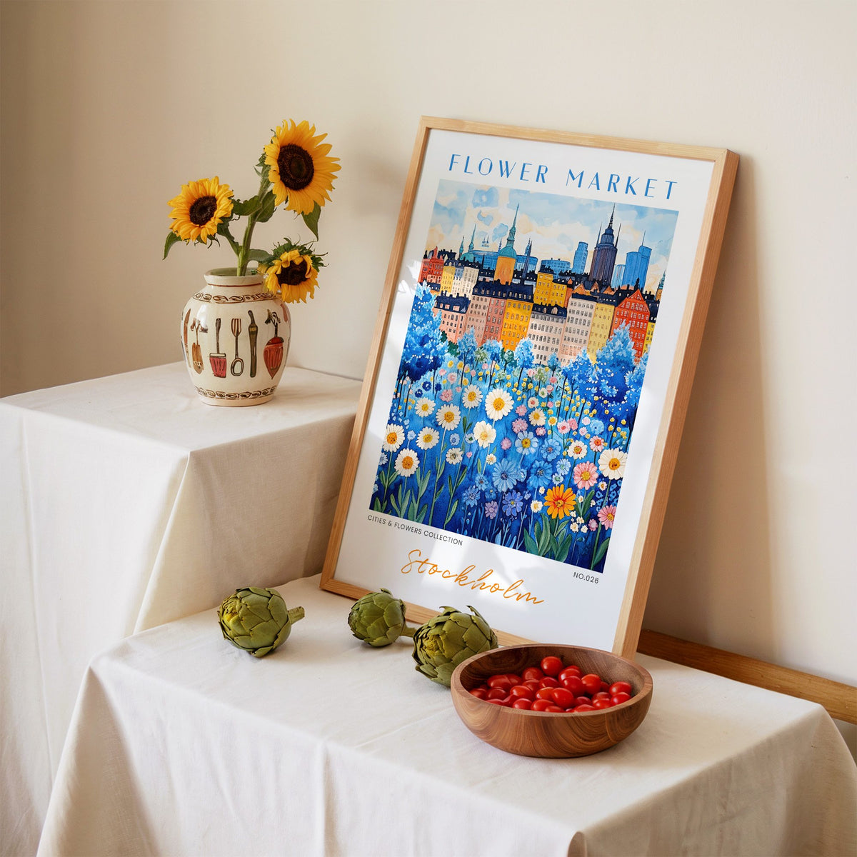 Stockholm flower market print in an oak frame leaning on a linen-draped table beside a vase of sunflowers