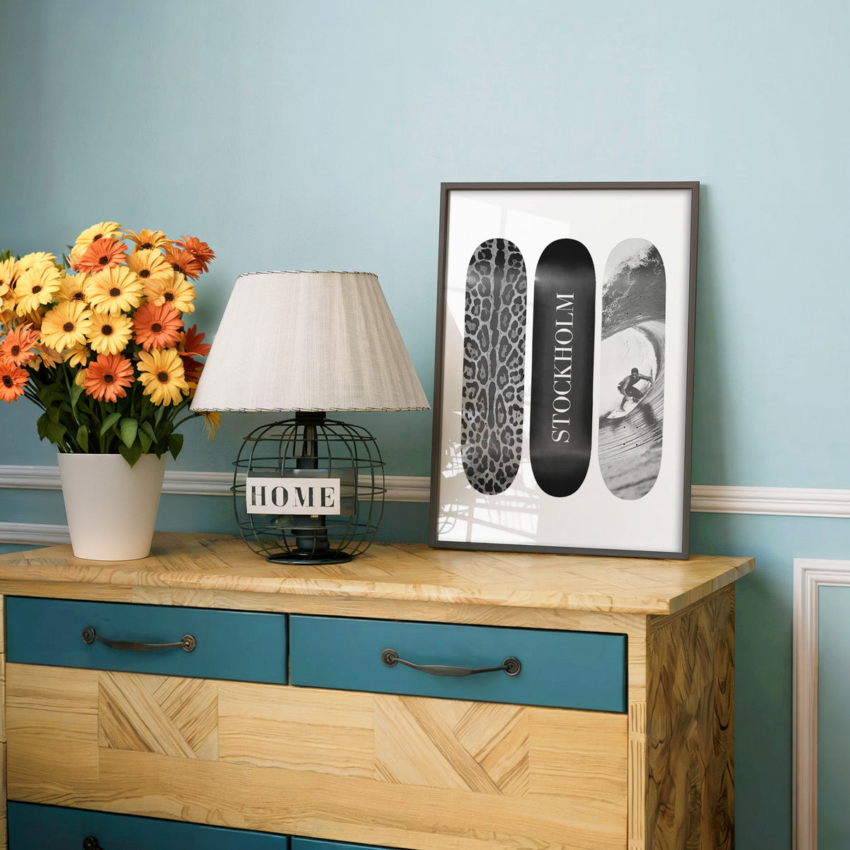 Three skateboards with leopard spots, Stockholm deck, surfer in a charcoal frame on a teal dresser beside orange daisies
