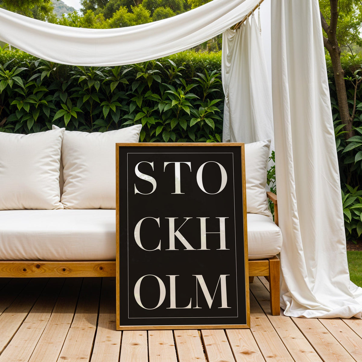 Stockholm stacked serif lettering on black print in an oak frame on an outdoor daybed under white drapes