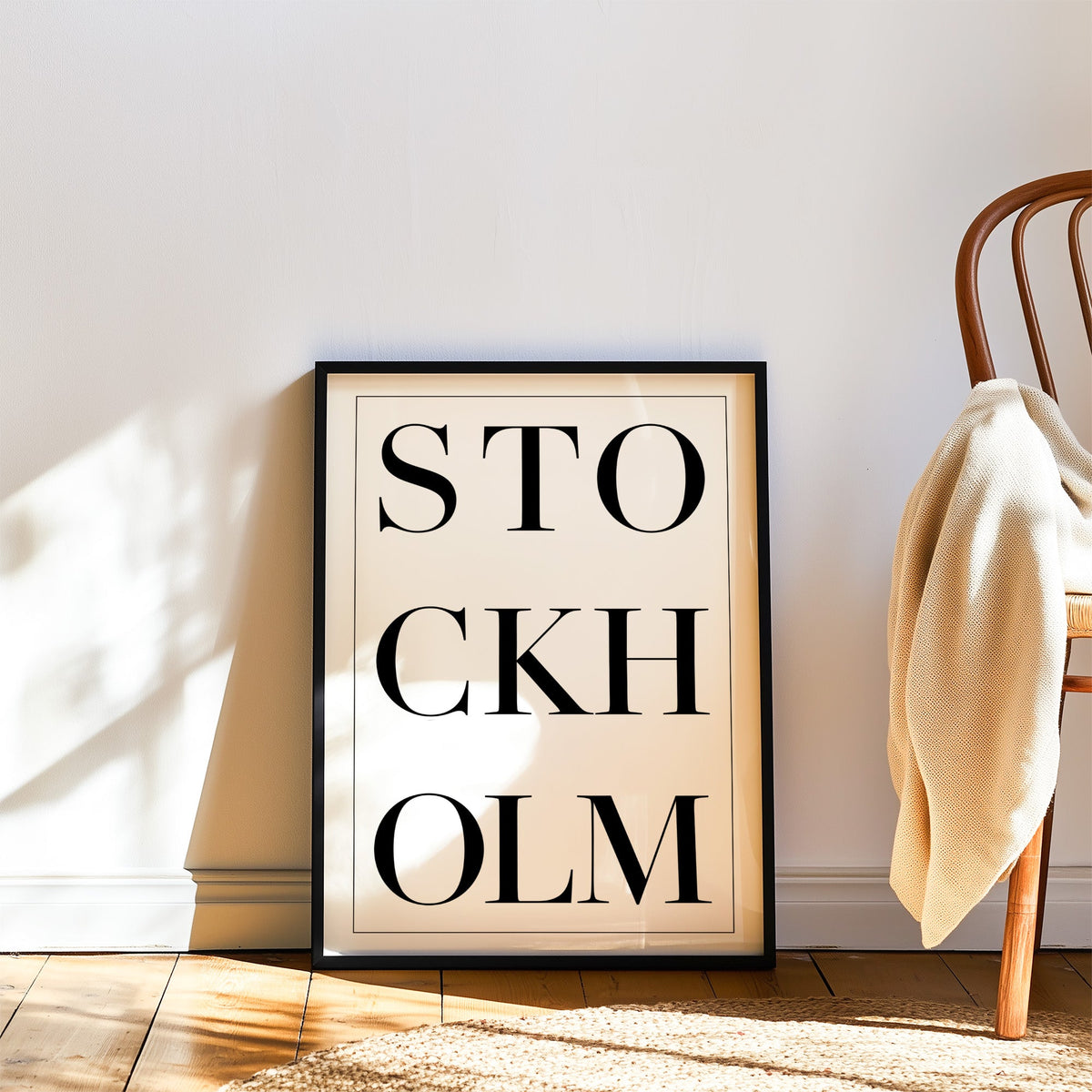 Stockholm stacked serif lettering on white print in a black frame leaning on a wood floor beside a bentwood chair